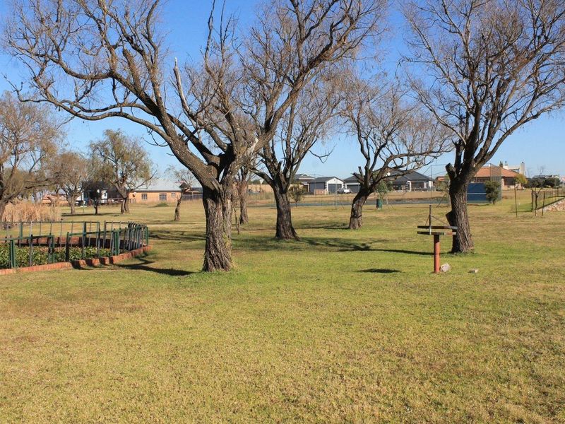 A spacious residential garden area featuring mature trees, a well-maintained lawn, and perimeter fencing, offering a peaceful outdoor setting.
