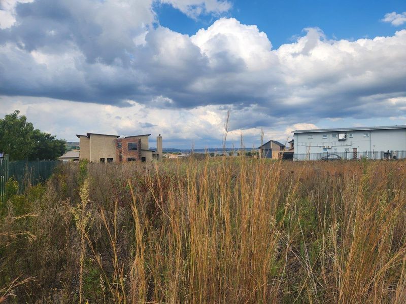 A vacant residential plot featuring overgrown grass and surrounding neighborhood development under a cloudy sky.