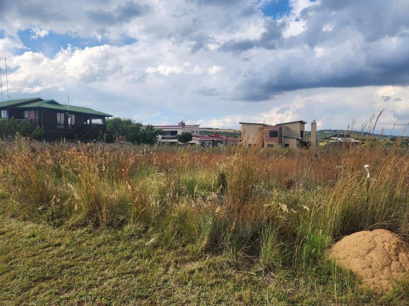 A view of a vacant residential plot featuring natural grassland with surrounding established residential properties in the background.