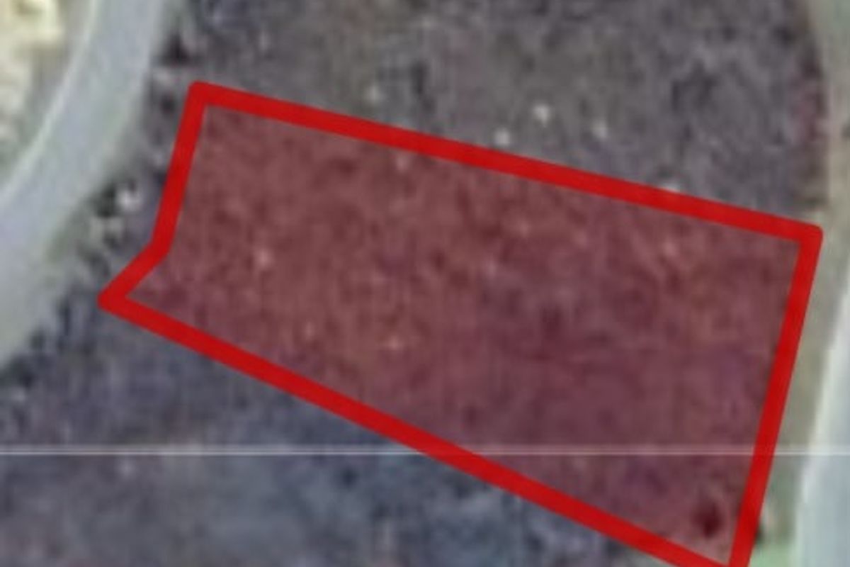 An aerial view of a vacant residential land plot highlighted with a red boundary line.