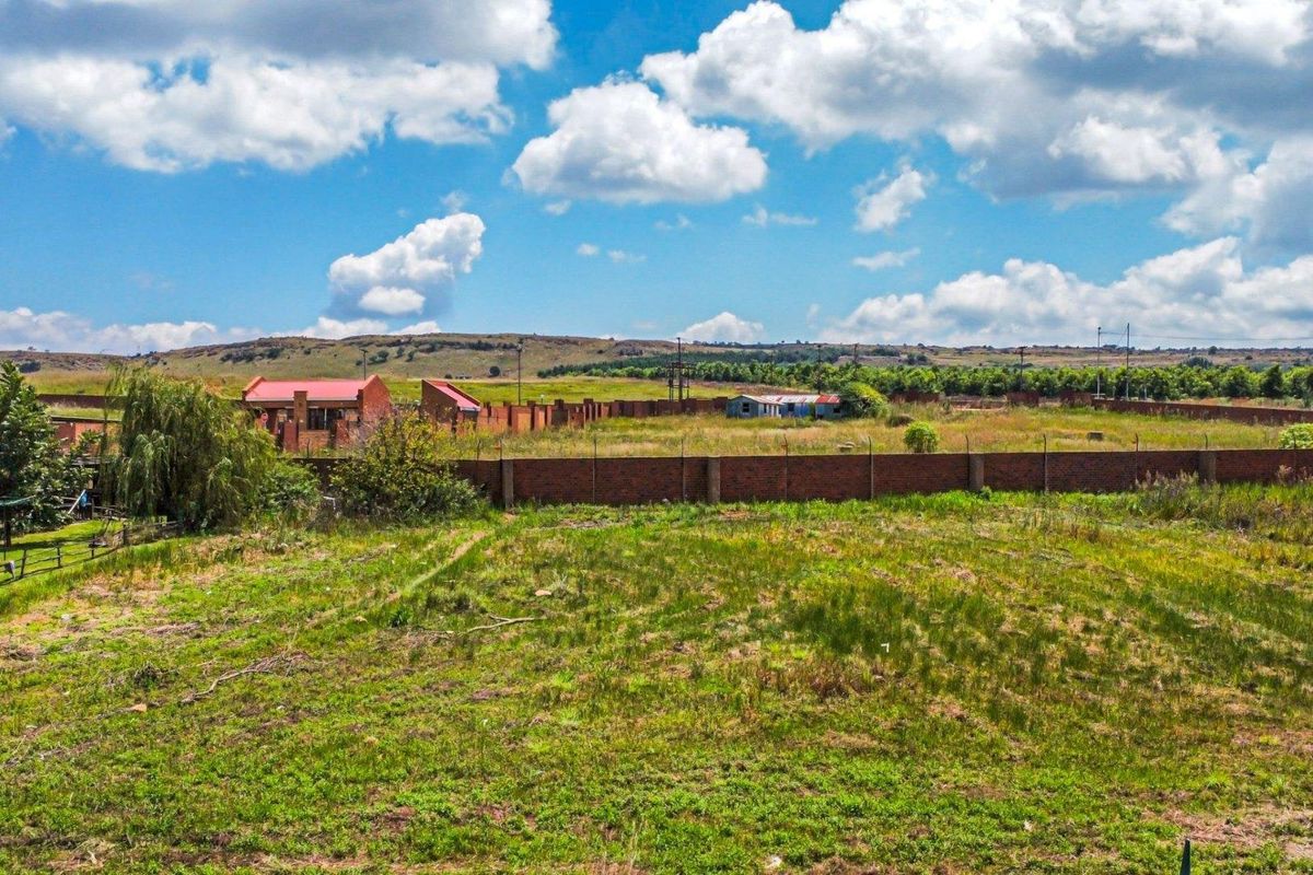 An aerial view of a vacant residential plot featuring a perimeter brick wall and surrounding landscape.