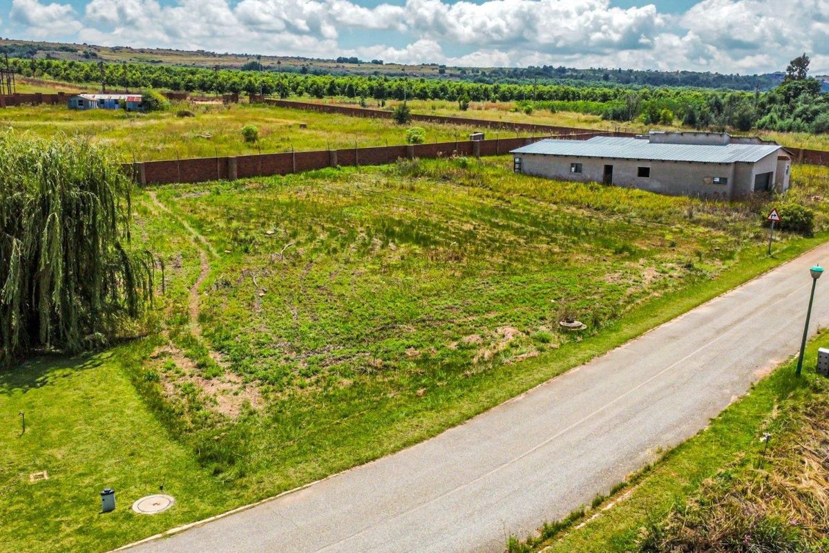 Aerial view of a vacant residential plot featuring an existing perimeter brick wall, adjacent asphalt road, and a small outbuilding structure.