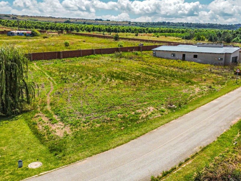 Aerial view of a vacant residential plot featuring an existing outbuilding, perimeter walling, and direct access to an asphalt road.