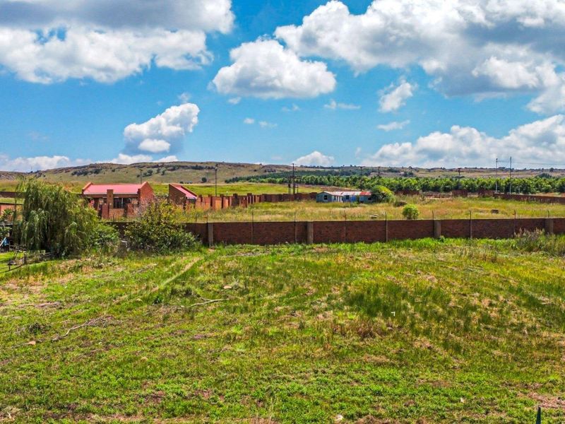 An aerial view of a vacant residential plot featuring perimeter brick walling and open grassland, suitable for future development.