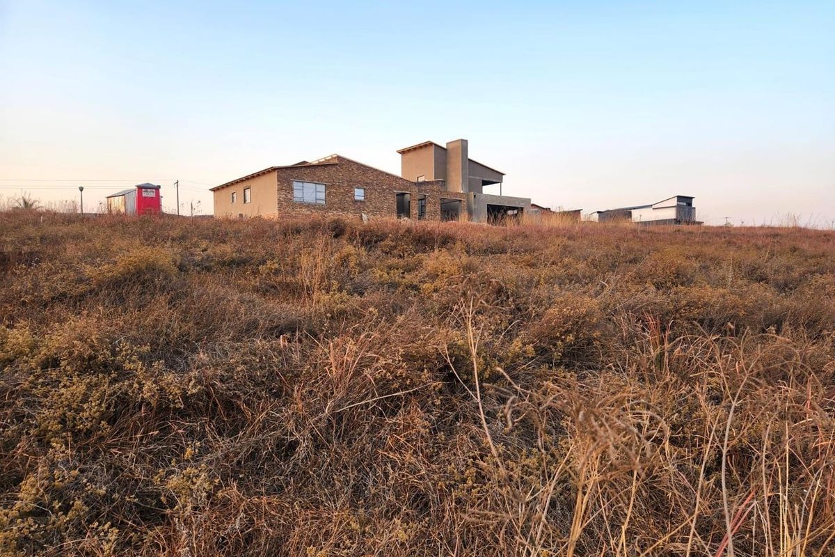 A view of a residential property under construction, featuring stone cladding and modern architectural lines set within a large, undeveloped grassy plot.