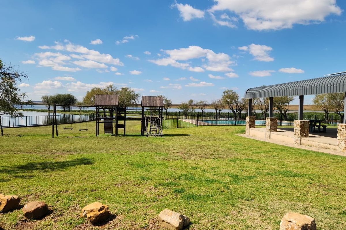 Spacious outdoor garden area featuring a covered patio, children's play equipment, and scenic water views in a tranquil residential setting.