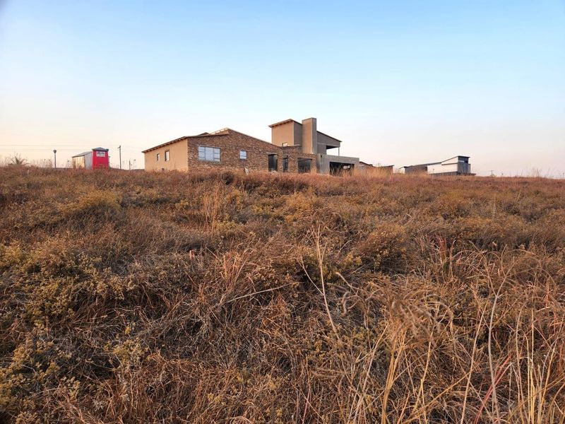 A view of a residential property under construction, featuring stone cladding and a modern architectural design set on a large vacant plot.
