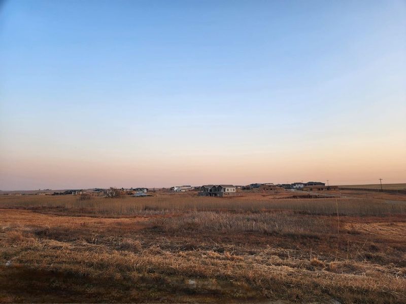A wide-angle view of an expansive vacant residential plot with distant housing developments visible on the horizon under a clear sky.