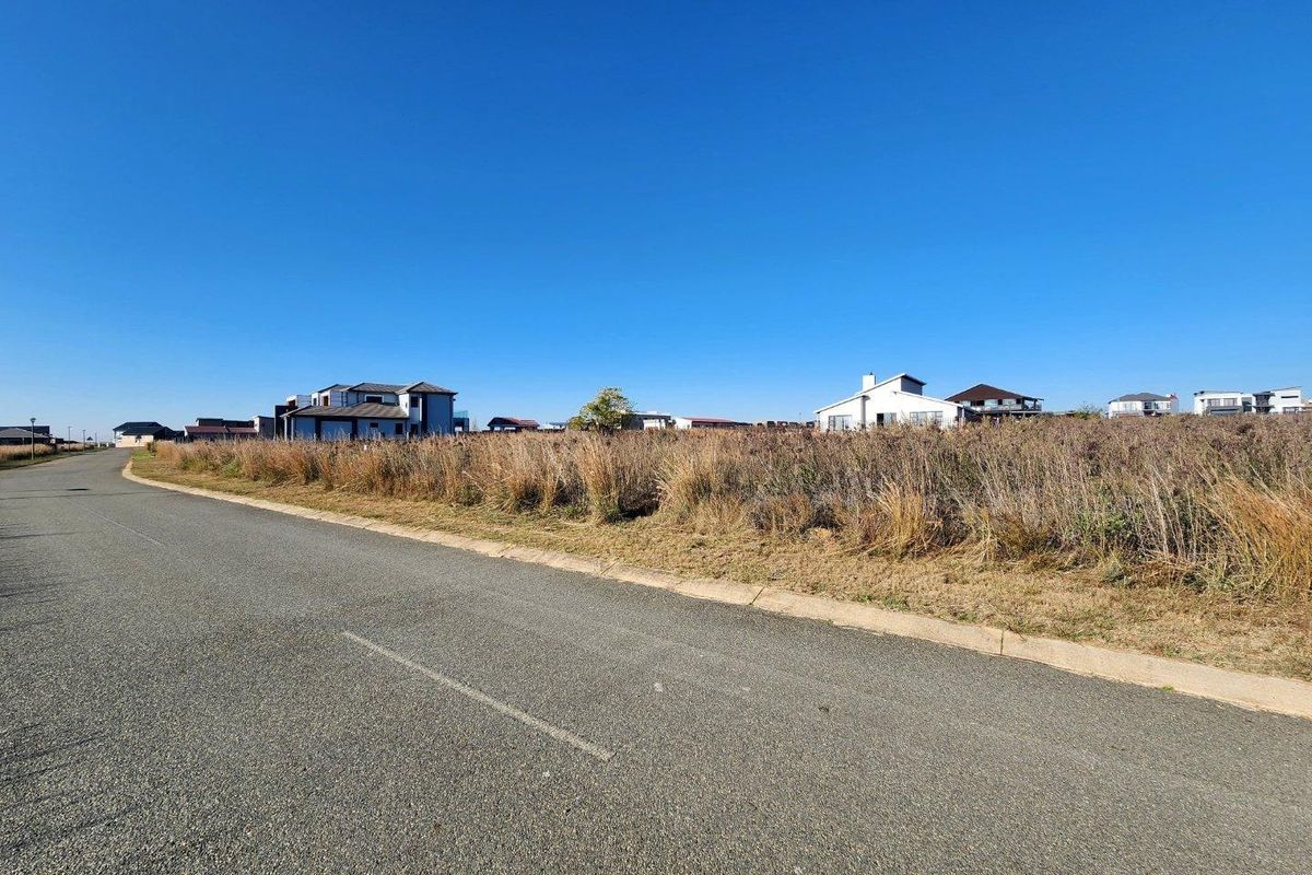 A view of the paved street and curb bordering the vacant residential land, with surrounding neighborhood homes visible in the distance.