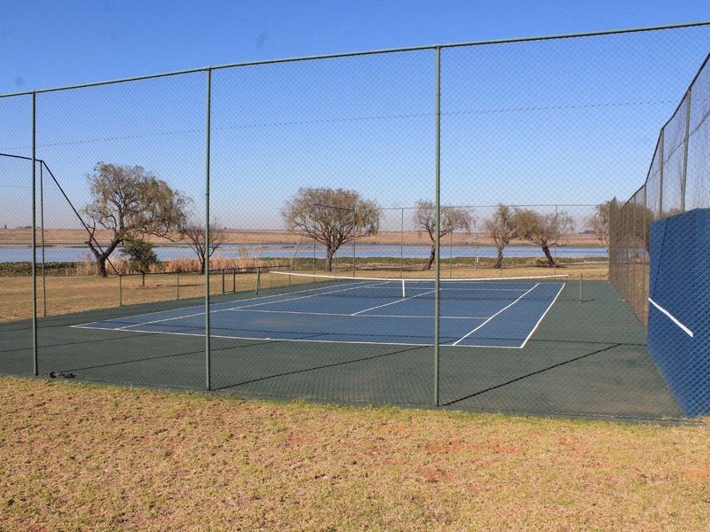 A well-maintained outdoor tennis court featuring a blue surface, enclosed by high chain-link fencing, set against a scenic landscape.