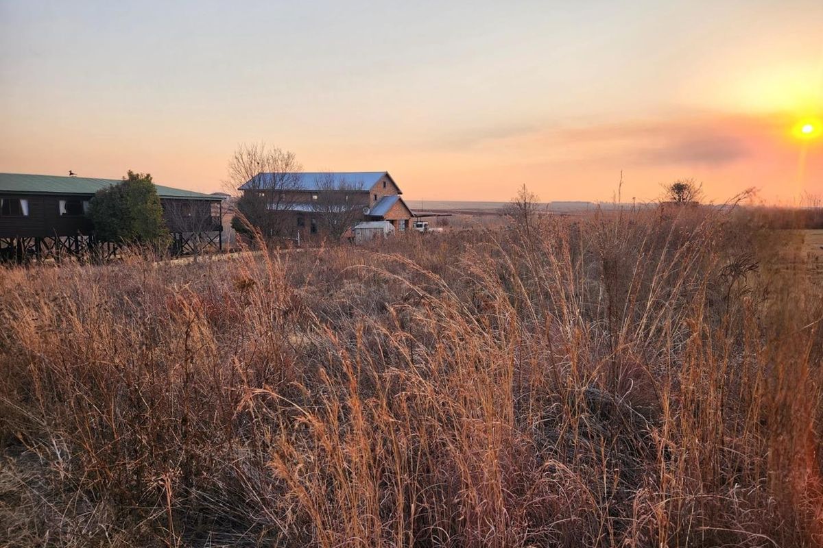 A scenic view of the residential property and surrounding landscape at sunset, featuring open fields and existing structures.