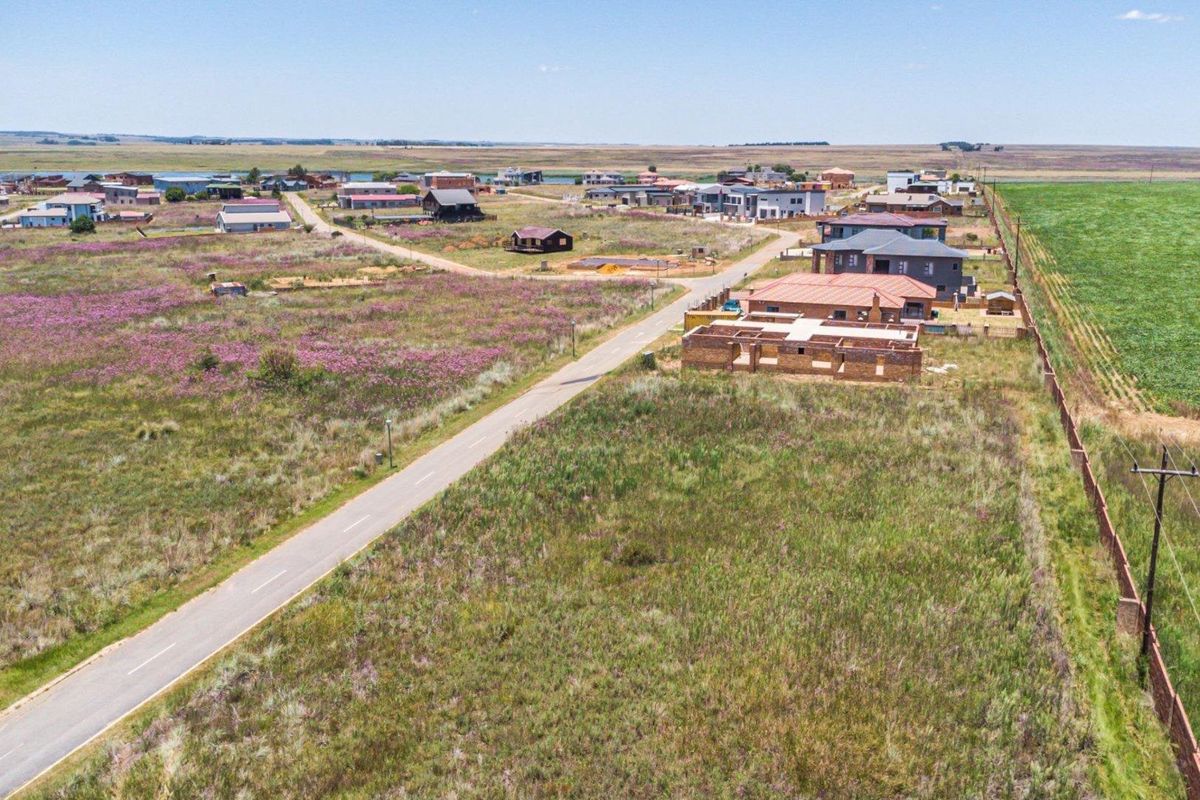 An aerial view of a residential development area featuring vacant land plots, paved roads, and surrounding rural landscape.