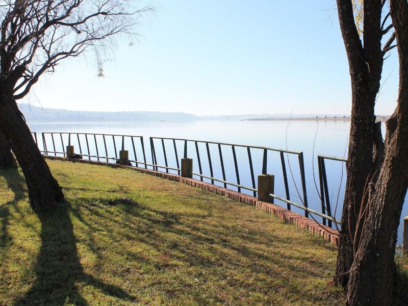 A scenic view of the waterfront featuring a grassy bank, a brick retaining wall, and a metal safety railing.