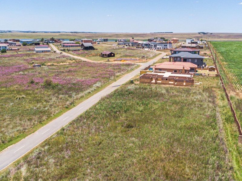 An aerial view of a residential development area featuring vacant land plots, paved roads, and surrounding rural landscape.