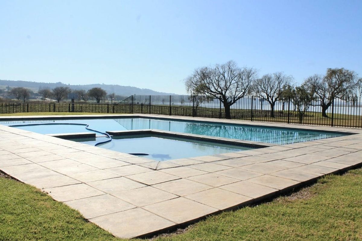 A well-maintained outdoor swimming pool area featuring a paved deck and metal perimeter fencing with scenic landscape views.