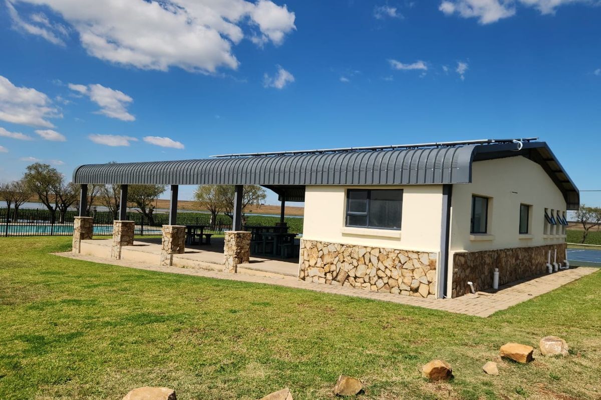 A spacious covered outdoor patio area featuring stone-clad pillars, a curved metal roof, and integrated solar panels, overlooking a landscaped garden.