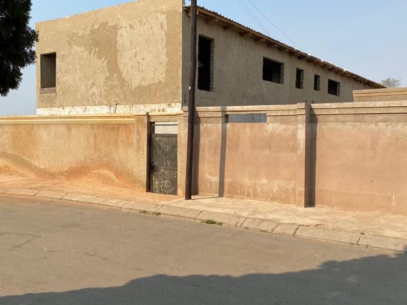Street view of an unfinished residential property featuring a boundary wall, metal gate, and unrendered masonry exterior.