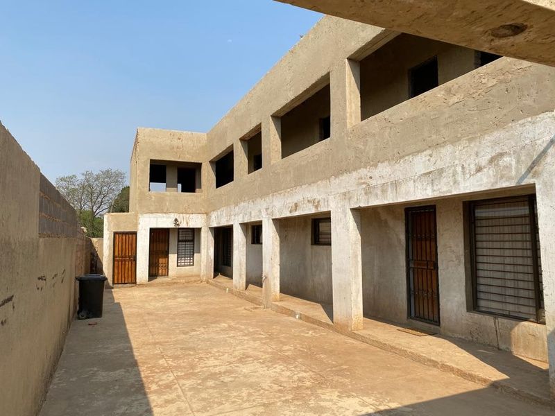 Rear view of a multi-story apartment building featuring unfinished concrete exterior walls, security gates, and a paved courtyard area.