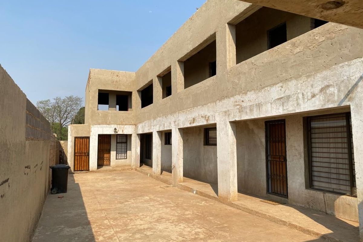 Rear view of a multi-story apartment building featuring unfinished concrete exterior walls, security gates, and a paved courtyard area.