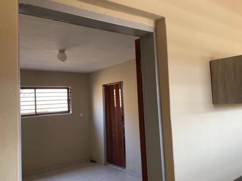 A simple, empty hallway area featuring tiled flooring, a folding door, and security bars on the window, presenting a functional transition space.
