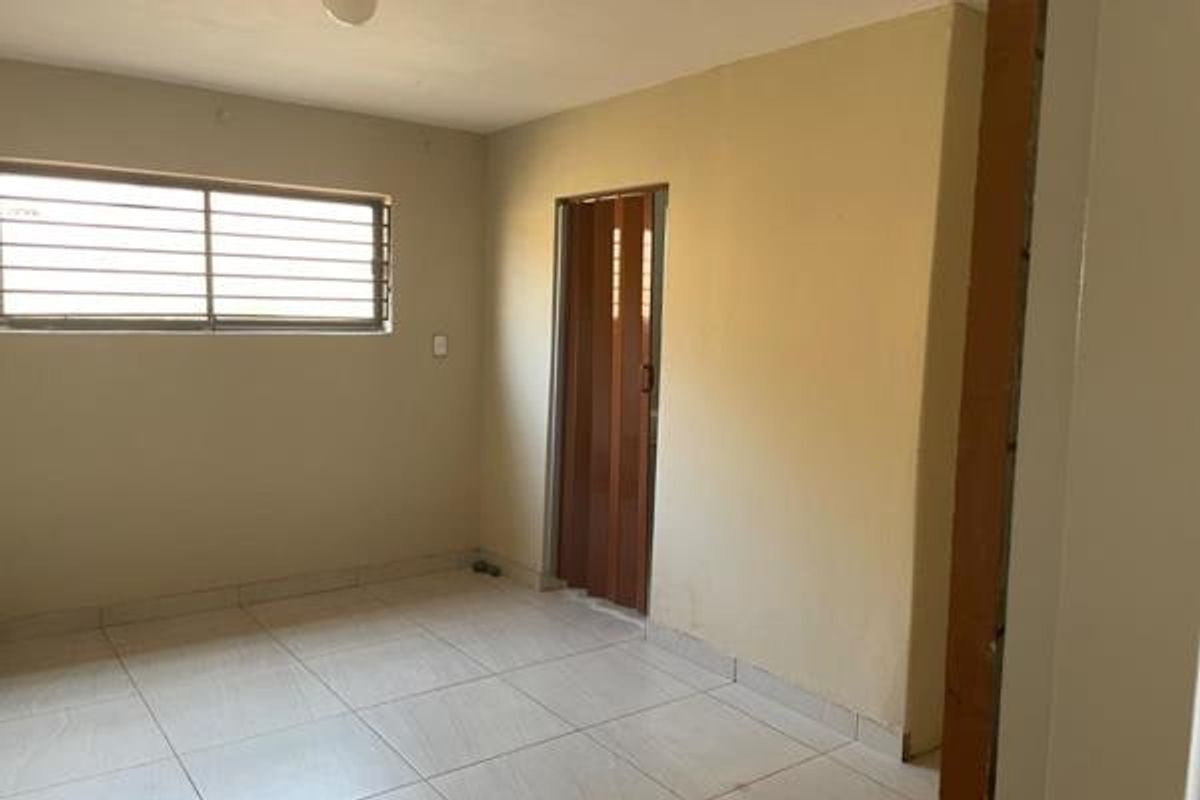 An empty bedroom featuring tiled flooring, a window with security bars, and a folding door, offering a blank canvas for renovation.