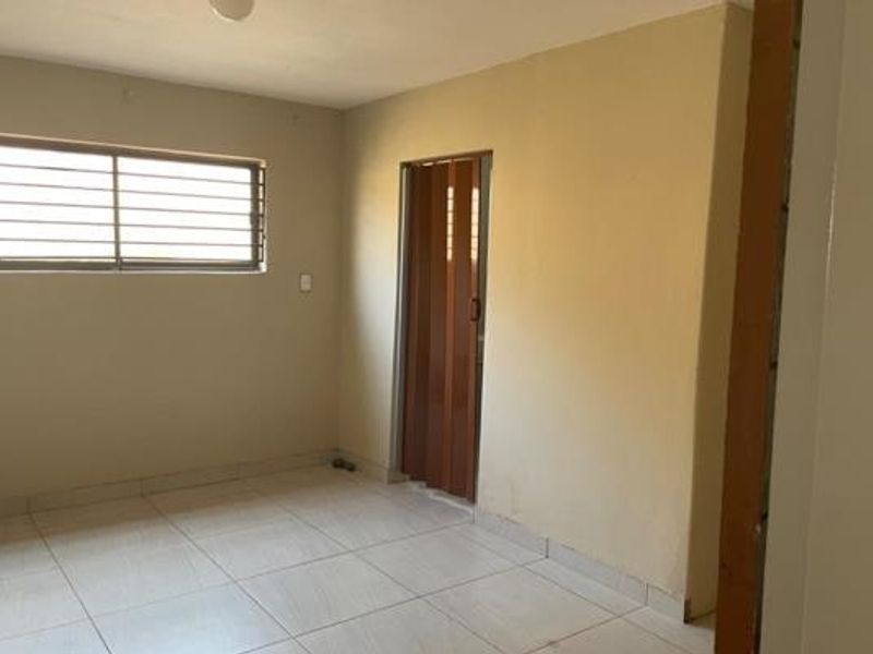 An empty bedroom featuring tiled flooring, a window with security bars, and a folding door, offering a blank canvas for renovation.