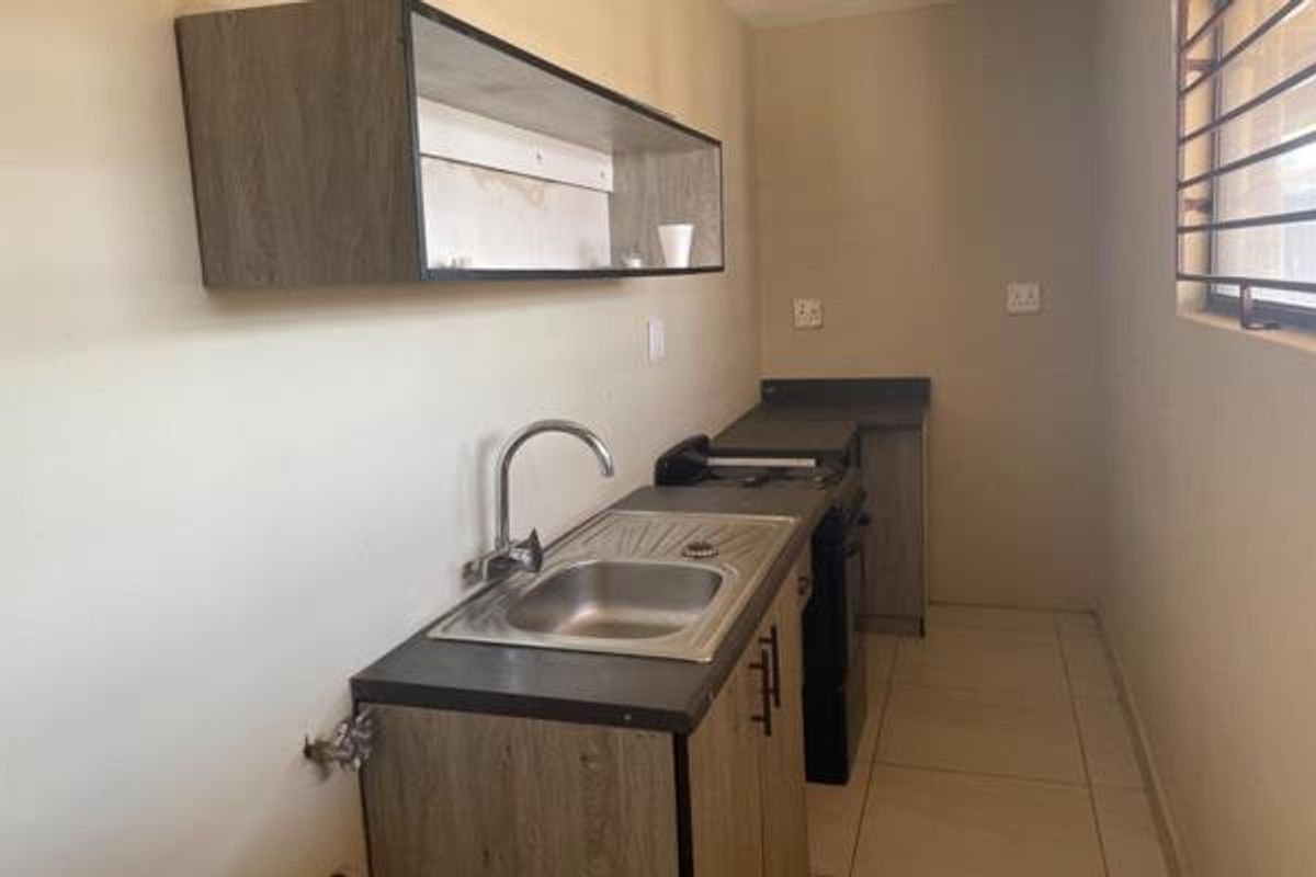 A compact kitchen area featuring built-in cabinetry, a stainless steel sink, and tiled flooring, offering a functional space ready for updates.