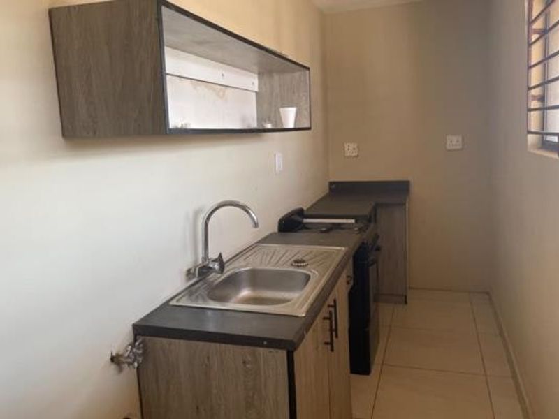 A compact kitchen area featuring built-in cabinetry, a stainless steel sink, and tiled flooring, offering a functional space ready for updates.