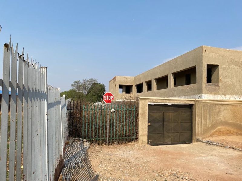 Exterior view of an unfinished apartment building featuring metal security fencing and a garage door, currently in a state of ongoing construction.