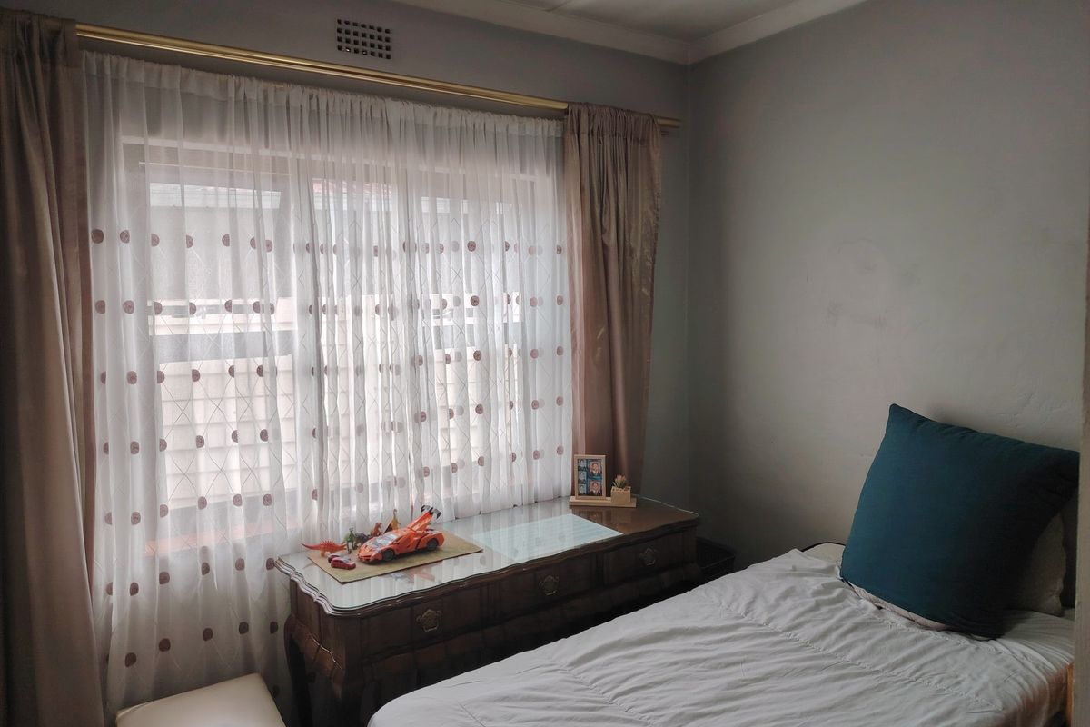 A cozy bedroom featuring a window with curtains and a ventilation grille, providing a comfortable and functional living space.