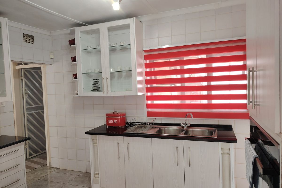 A functional kitchen featuring white cabinetry, granite countertops, a double bowl sink, and tiled splashbacks with a bright red window blind.