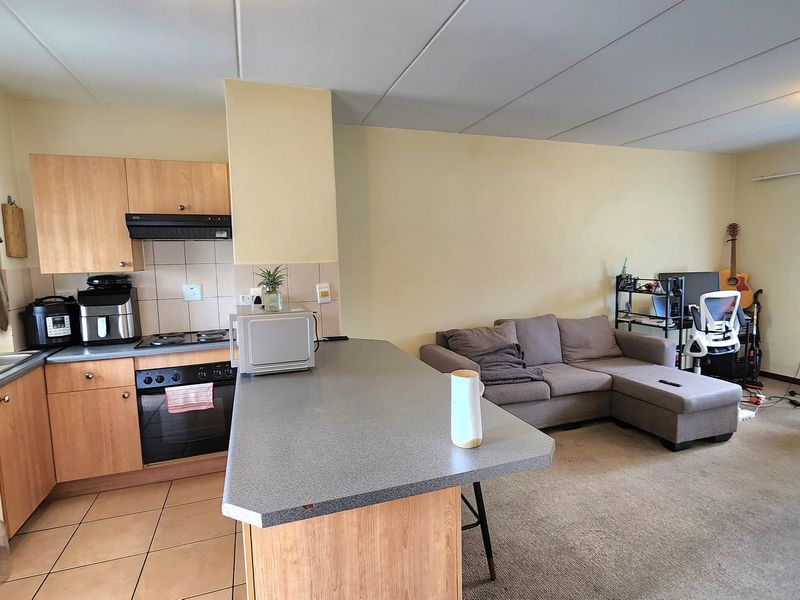 Open-plan kitchen and living area featuring wood-finish cabinetry, laminate countertops, built-in oven, and a breakfast bar, transitioning into a carpeted lounge space.