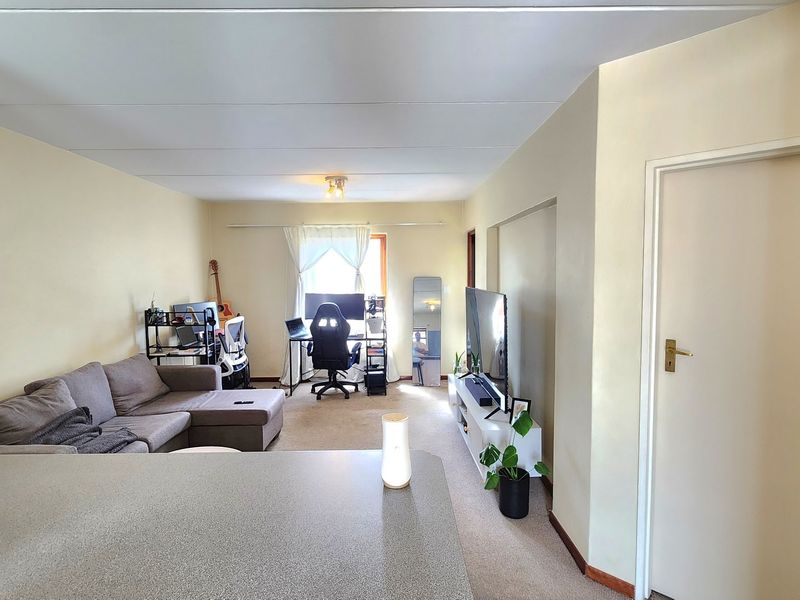 Open-plan living area featuring neutral walls, carpeted flooring, and a functional layout connecting to the kitchen space.