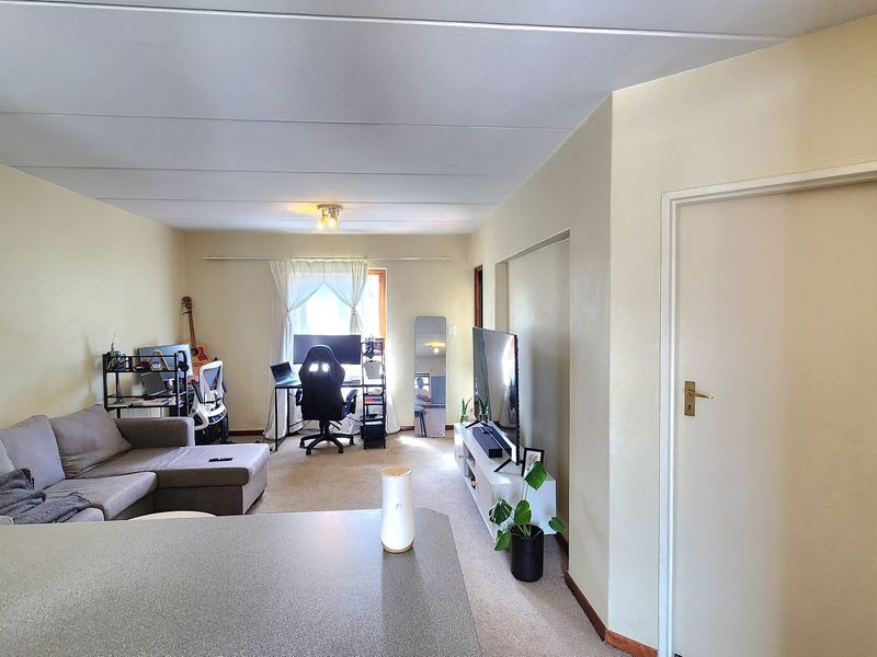 Open plan living area featuring neutral wall finishes, carpeted flooring, and a functional layout suitable for combined lounge and workspace use.