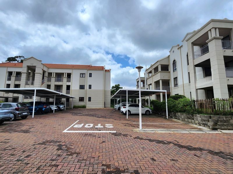 Exterior view of an apartment complex featuring paved parking areas with covered carports and multi-story residential buildings with balconies.