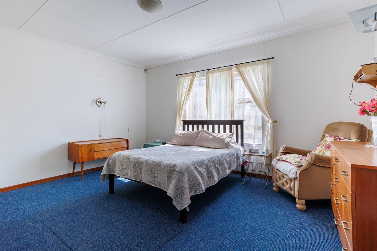 A spacious bedroom featuring blue carpeting and a large window with curtain rods, offering a neutral canvas for potential updates.