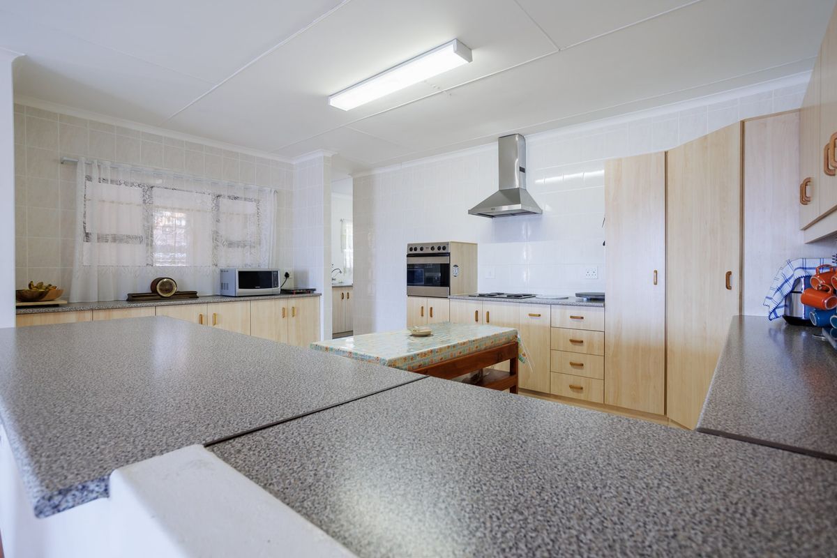 A functional kitchen featuring laminate cabinetry, ample countertop space, a built-in oven, hob, and stainless steel extractor fan with tiled splashbacks.