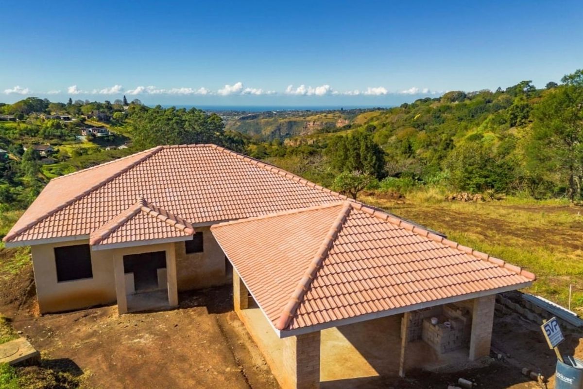 Aerial view of a residential property under construction, featuring a completed terracotta tiled roof and expansive surrounding landscape views.
