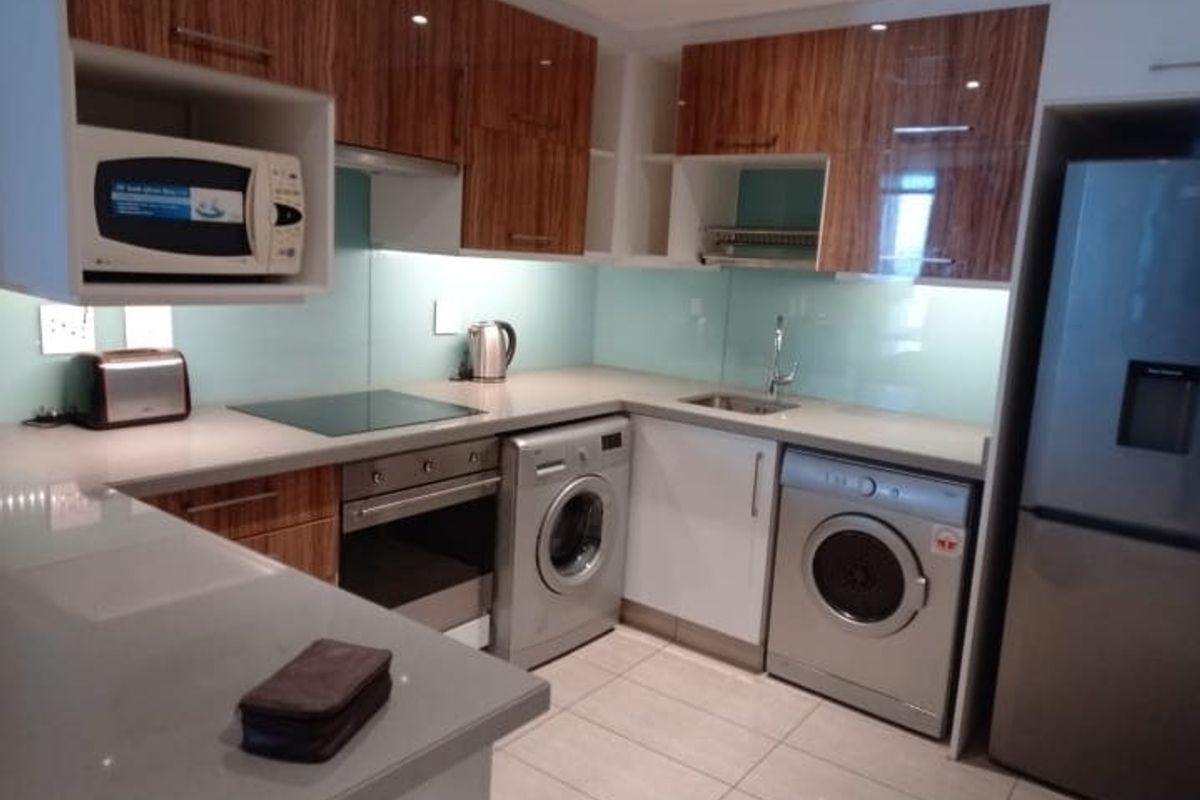 Modern kitchen featuring high-gloss wood-grain cabinetry, stone countertops, glass splashback, and integrated appliances including an oven, hob, and extractor fan.