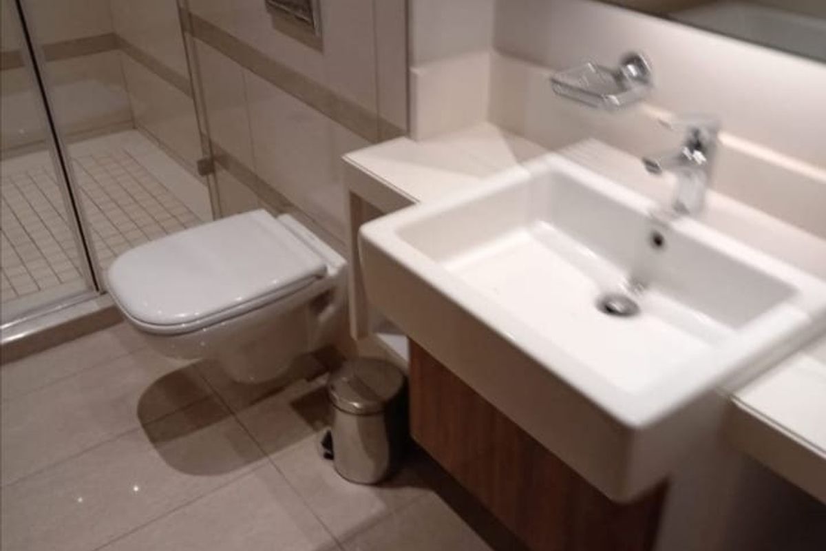 A modern bathroom featuring a wall-mounted toilet, a glass-enclosed shower, and a sleek vanity basin with a chrome mixer tap.