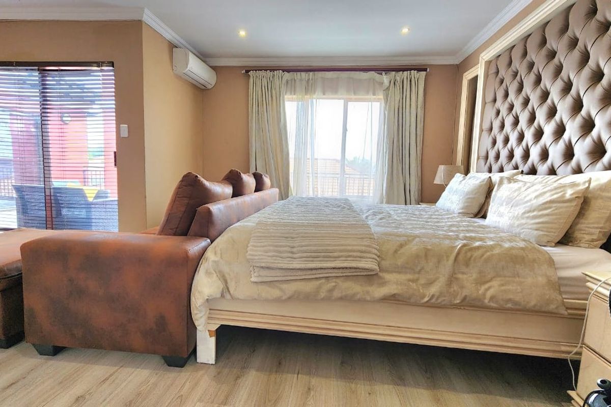 Spacious bedroom featuring laminate flooring, a large tufted headboard, split-system air conditioning, and direct access to an outdoor patio area.