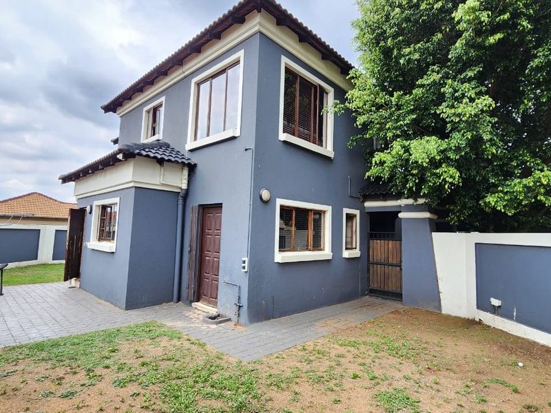 Rear view of a two-story residential property featuring a paved patio area, boundary walls, and established garden space.