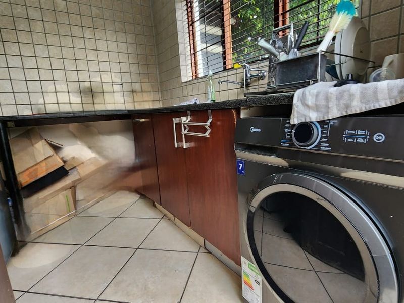 A functional laundry area featuring tiled splashbacks, granite countertops, and built-in cabinetry with space for a washing machine.