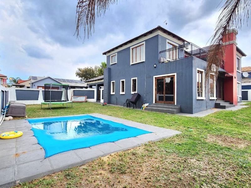 Rear view of a two-story house featuring a swimming pool, paved surround, balcony, and a private garden enclosed by perimeter walls.