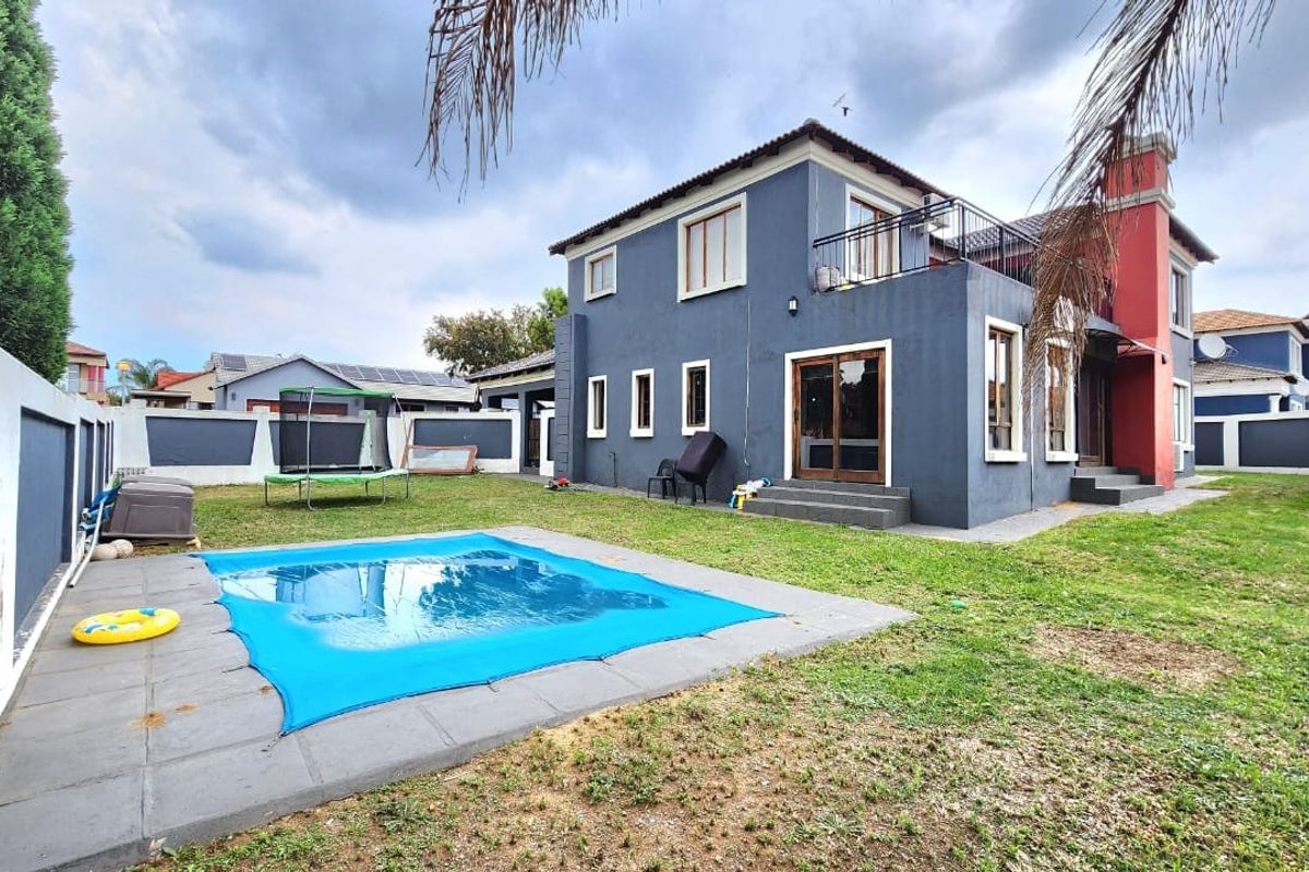 Rear view of a two-story house featuring a swimming pool, paved surround, balcony, and a private garden enclosed by perimeter walls.