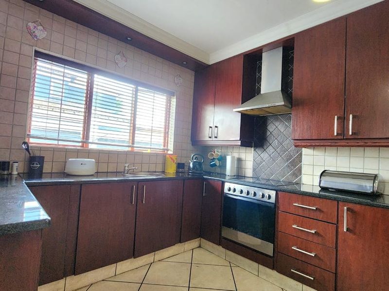 A functional kitchen featuring dark wood cabinetry, granite countertops, a built-in oven with extractor fan, and tiled flooring.
