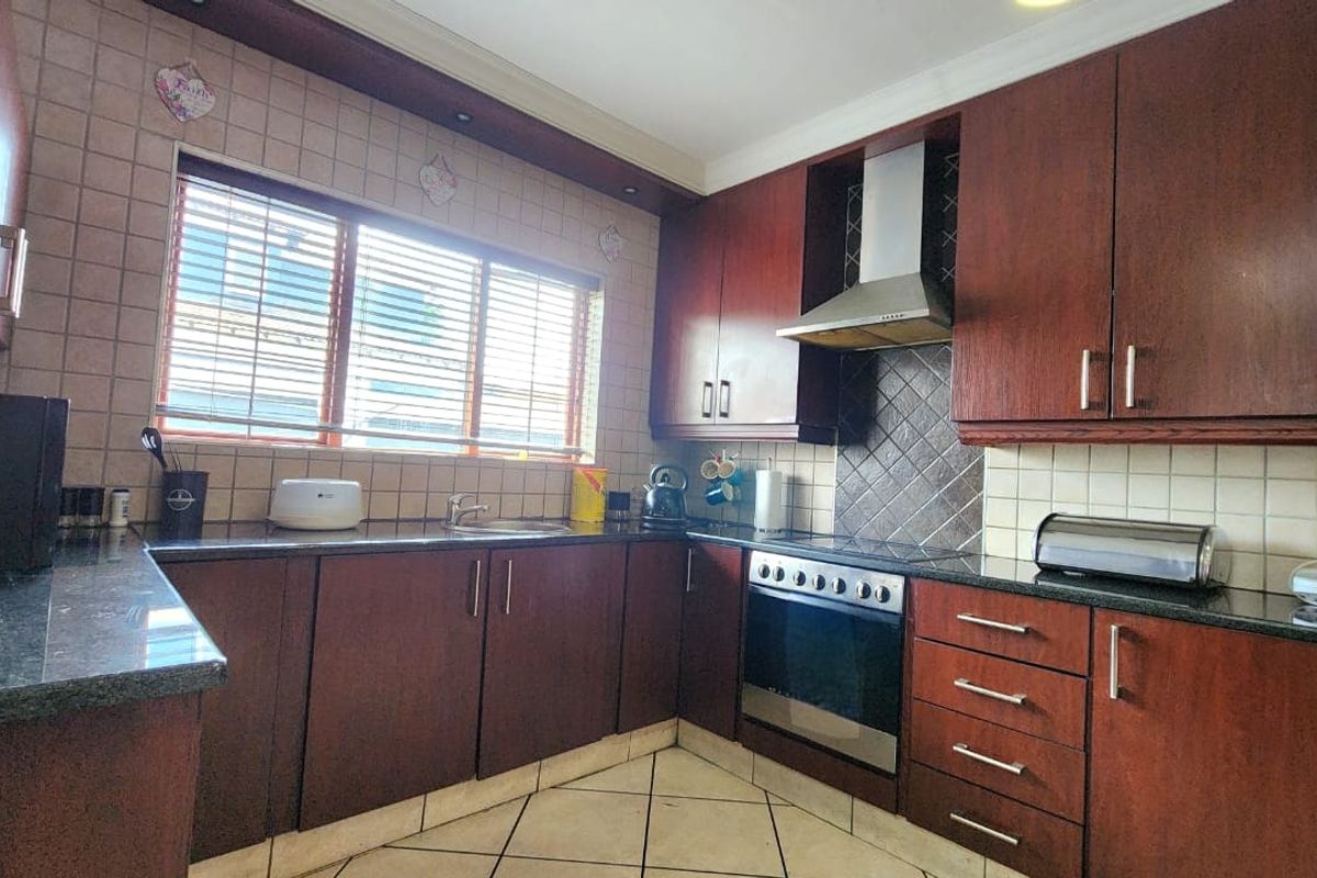 A functional kitchen featuring dark wood cabinetry, granite countertops, a built-in oven with extractor fan, and tiled flooring.