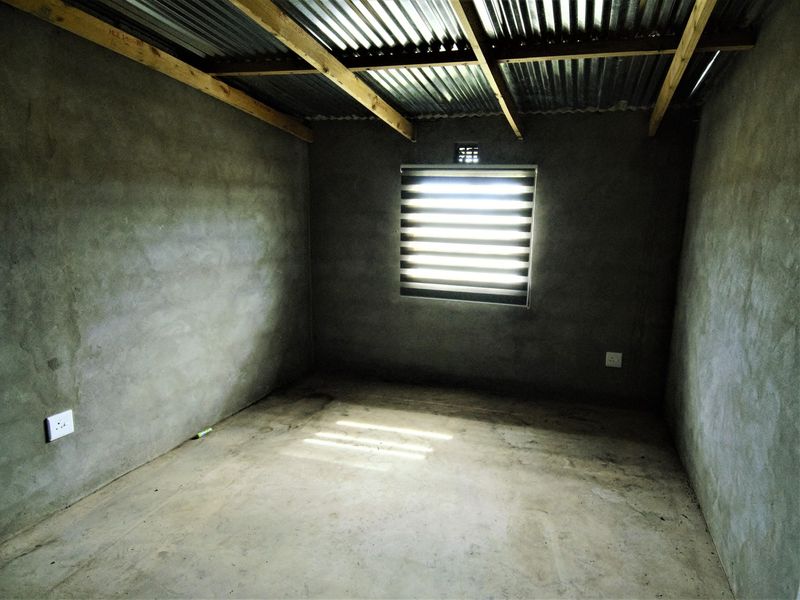 An unfinished bedroom space featuring exposed timber rafters, corrugated metal roofing, and raw cement wall and floor finishes.