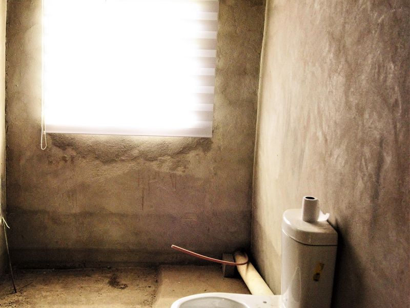 An unfinished bathroom space featuring a toilet and roller blind, currently in a shell condition requiring wall and floor finishing.