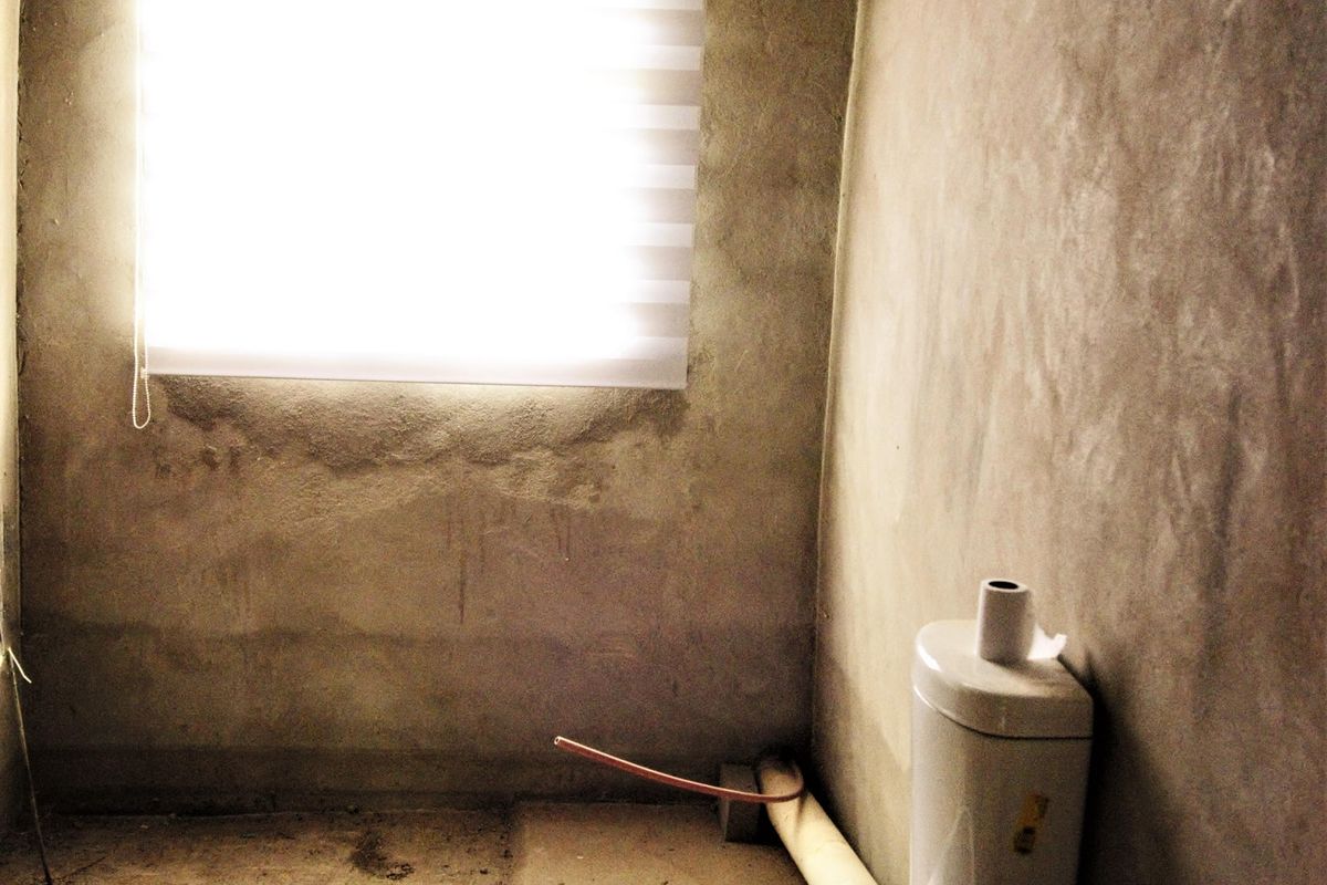 An unfinished bathroom space featuring a toilet and roller blind, currently in a shell condition requiring wall and floor finishing.
